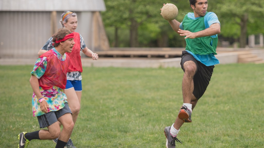 A student holding a ball about to jump and throw it.